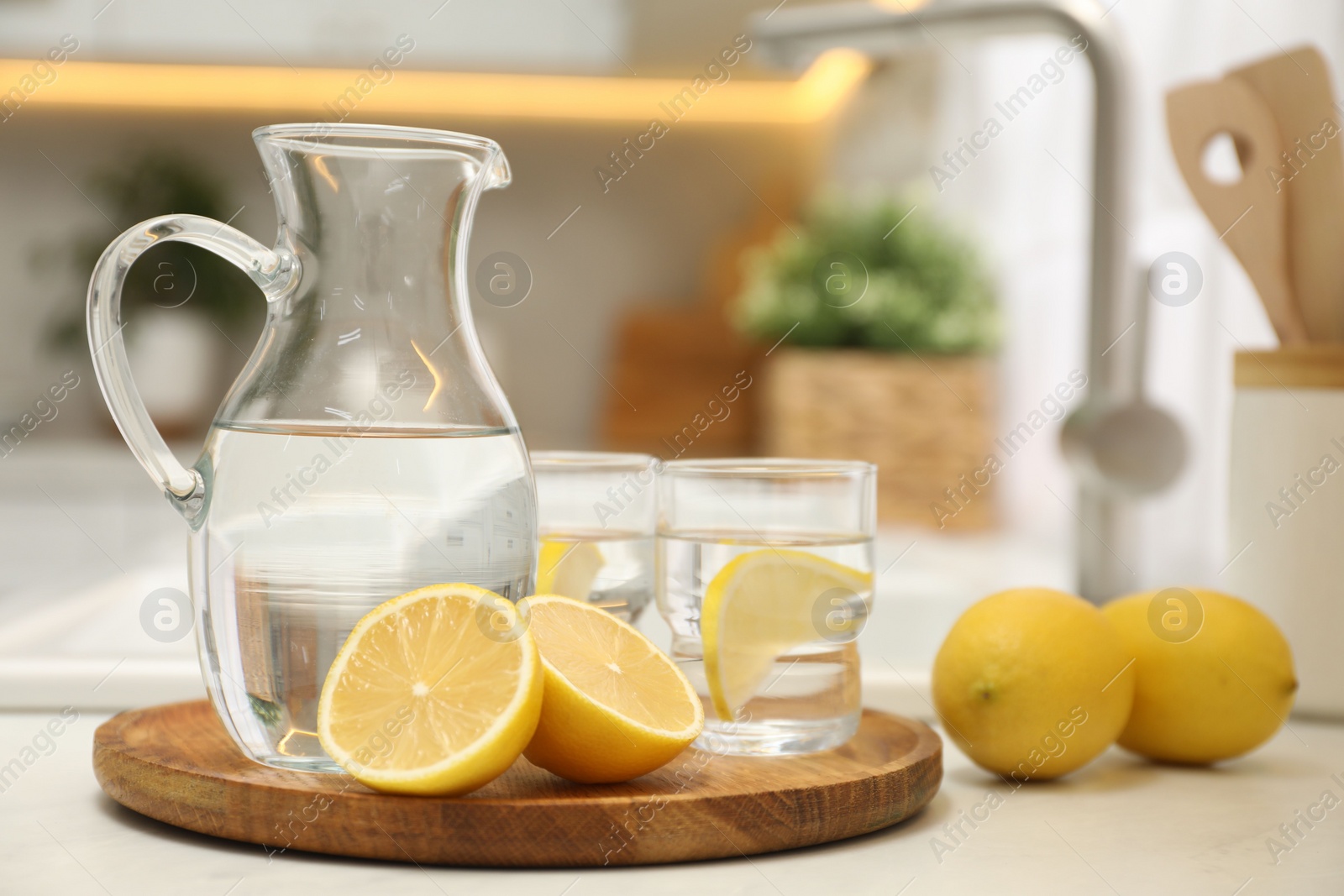 Photo of Jug, glasses with clear water and lemons on white table in kitchen