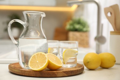 Photo of Jug, glasses with clear water and lemons on white table in kitchen