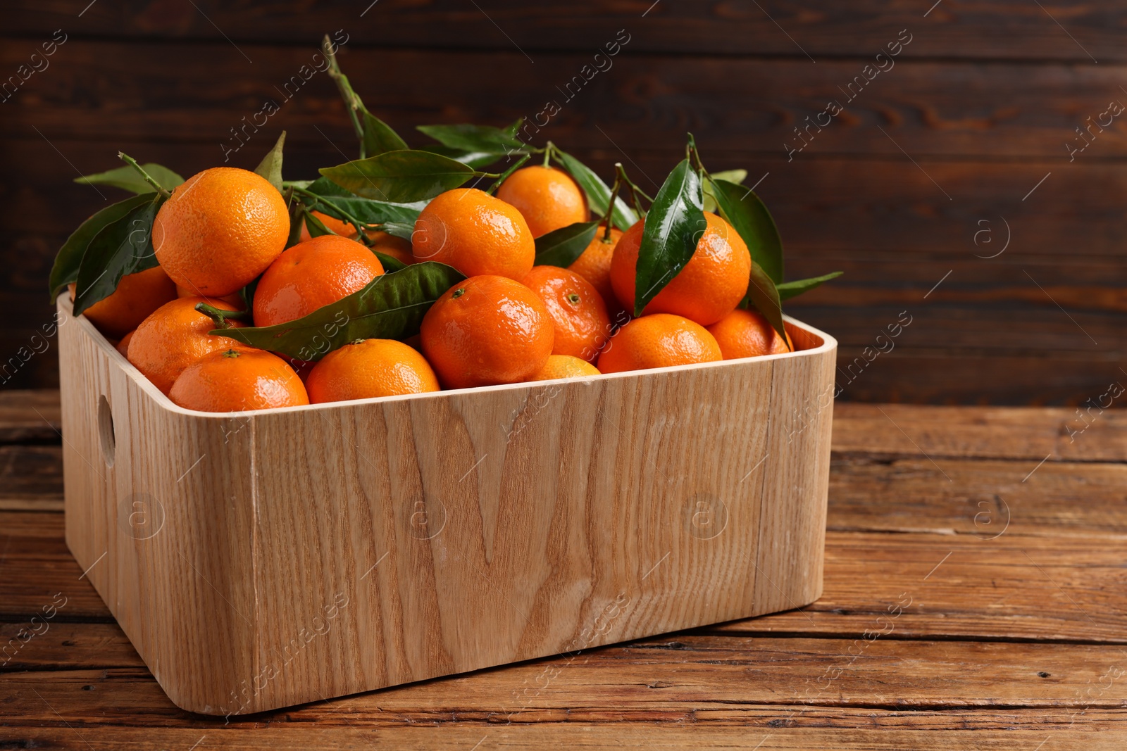 Photo of Fresh tangerines with green leaves in crate on wooden table