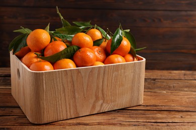 Fresh tangerines with green leaves in crate on wooden table