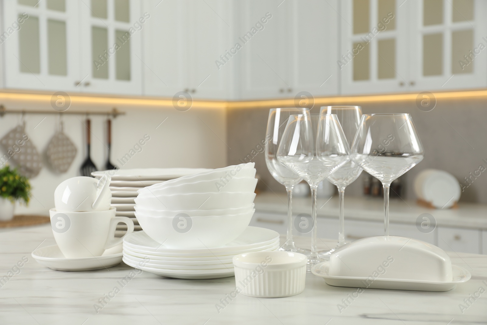 Photo of Clean plates, bowls, cups and glasses on white marble table in kitchen