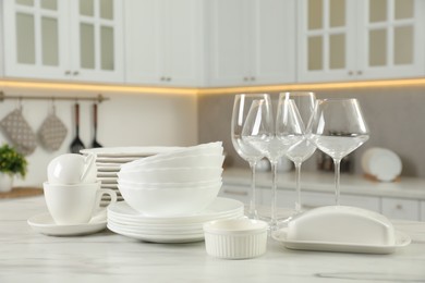 Clean plates, bowls, cups and glasses on white marble table in kitchen