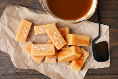 Delicious candies with sea salt and caramel sauce on wooden table, flat lay