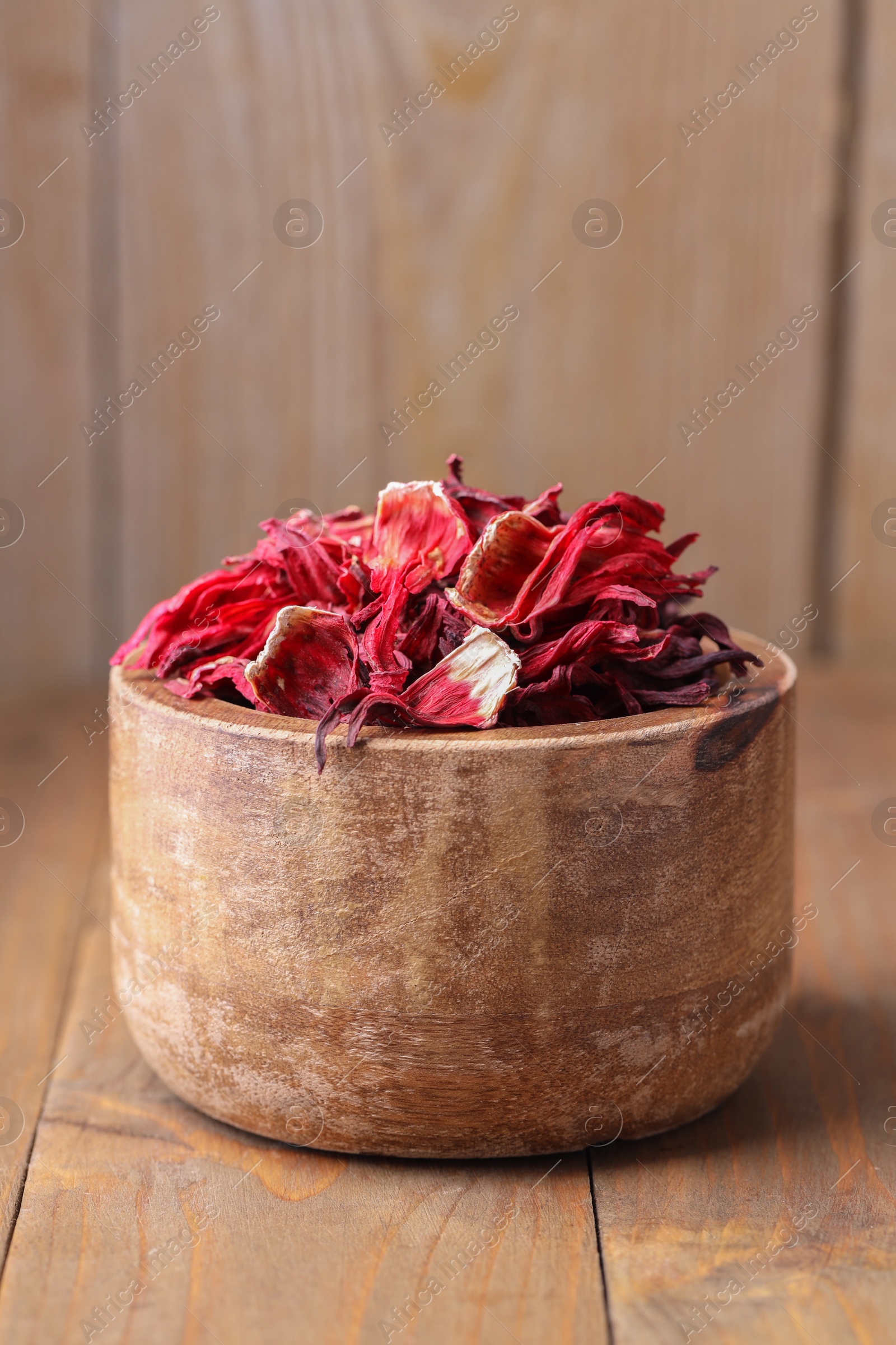 Photo of Dry hibiscus tea in bowl on wooden table, closeup