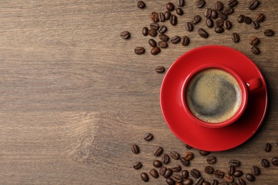 Photo of Cup of aromatic coffee and beans on wooden table, flat lay. Space for text