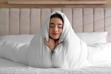 Photo of Beautiful young woman covered with warm blanket on bed at home