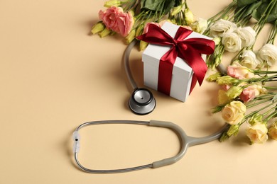 Stethoscope, gift box and flowers on beige background. Happy Doctor's Day