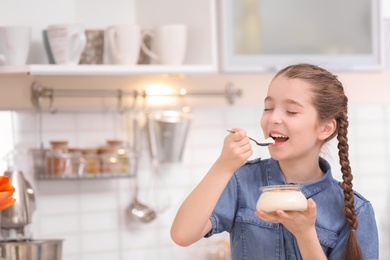 Cute girl eating tasty yogurt in kitchen