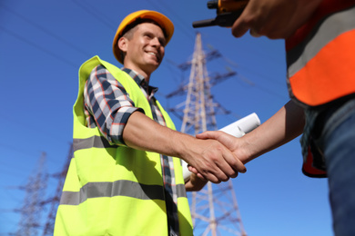 Photo of Professional electricians shaking hands near high voltage tower, closeup