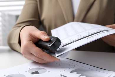 Photo of Woman with documents using stapler at white table indoors, closeup