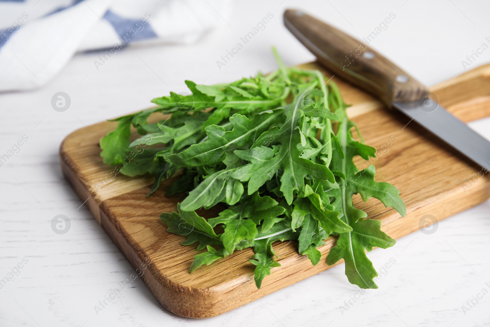 Photo of Fresh arugula, cutting board and knife on white wooden table