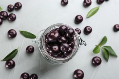 Photo of Jar with fresh acai berries and green leaves on light grey table, flat lay
