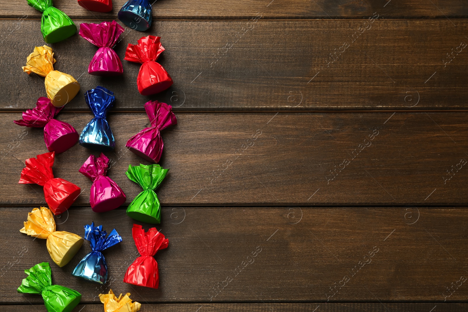 Photo of Many candies in colorful wrappers on wooden table, flat lay. Space for text