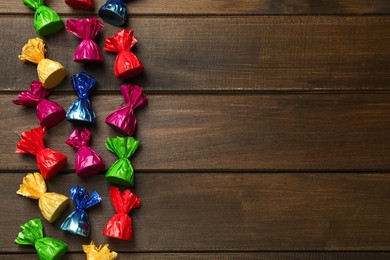 Many candies in colorful wrappers on wooden table, flat lay. Space for text