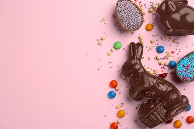 Photo of Flat lay composition with chocolate Easter bunnies, eggs and candies on pink background. Space for text