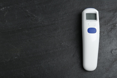 Photo of Modern non-contact infrared thermometer on black slate background, top view. Space for text