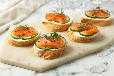 Tasty canapes with salmon, cucumber and cream cheese on white marble table, closeup