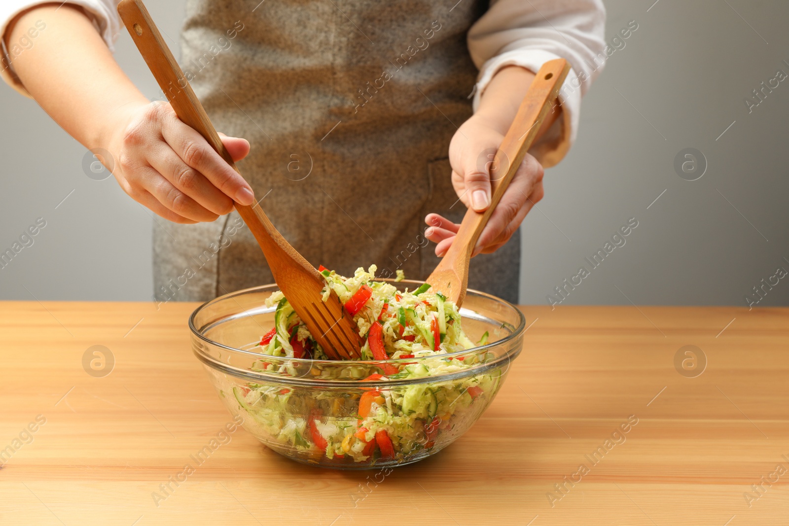 Photo of Woman making tasty salad with Chinese cabbage at wooden table, closeup