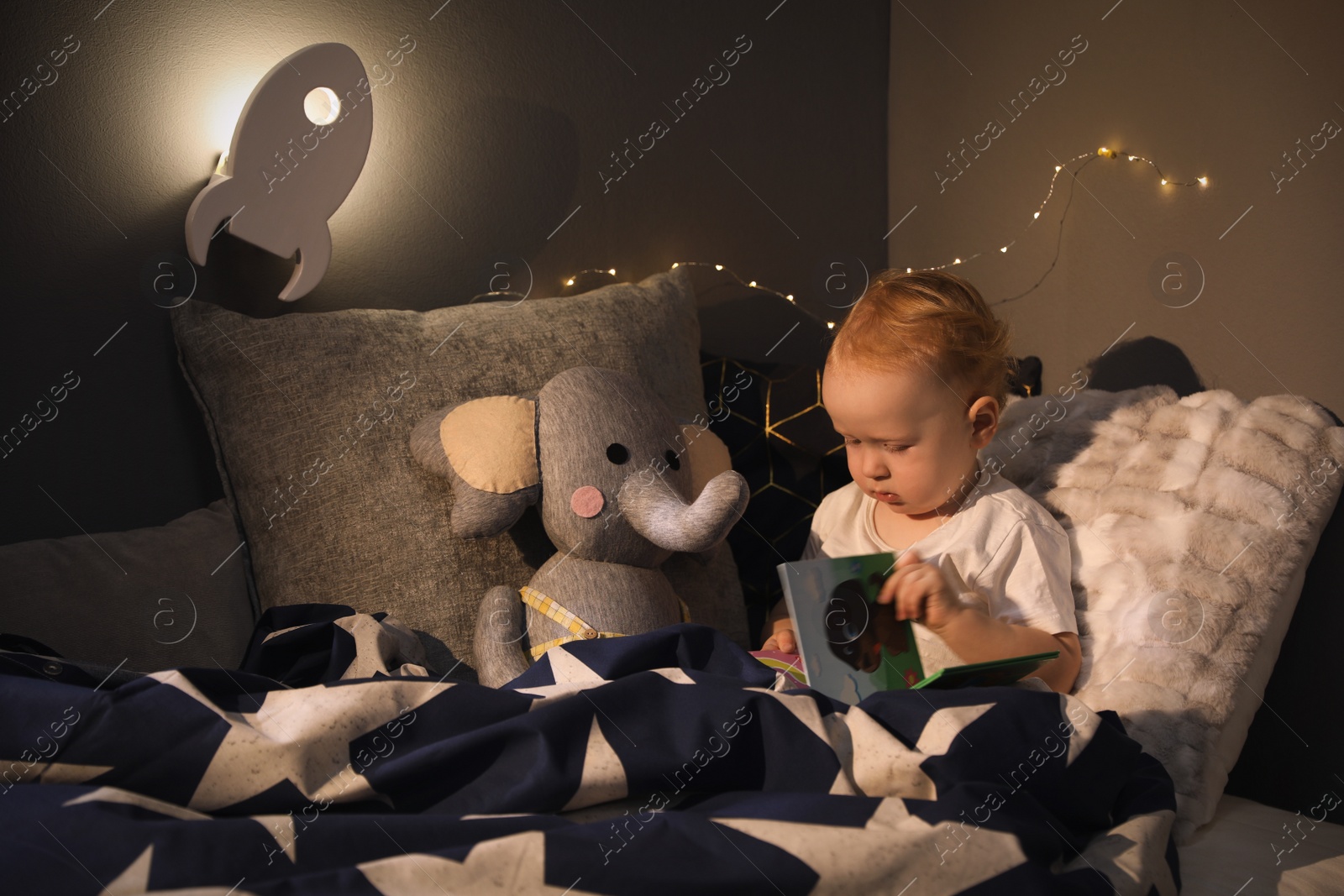 Photo of Cute child in room with rocket shaped night lamp