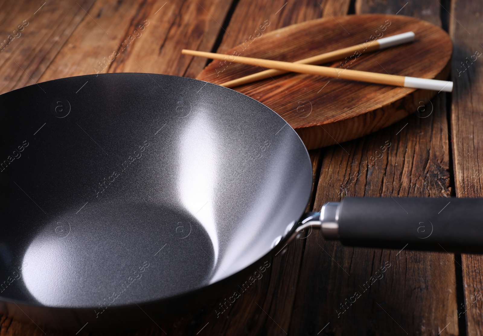 Photo of Empty iron wok and chopsticks on wooden table, closeup