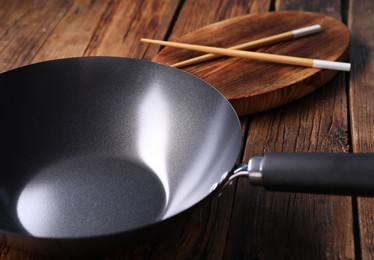 Photo of Empty iron wok and chopsticks on wooden table, closeup