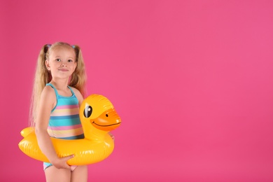 Cute little child in beachwear with bright inflatable ring on pink background. Space for text