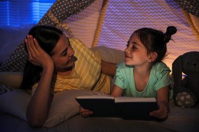 Photo of Little girl with mother reading fairy tale in play tent at home