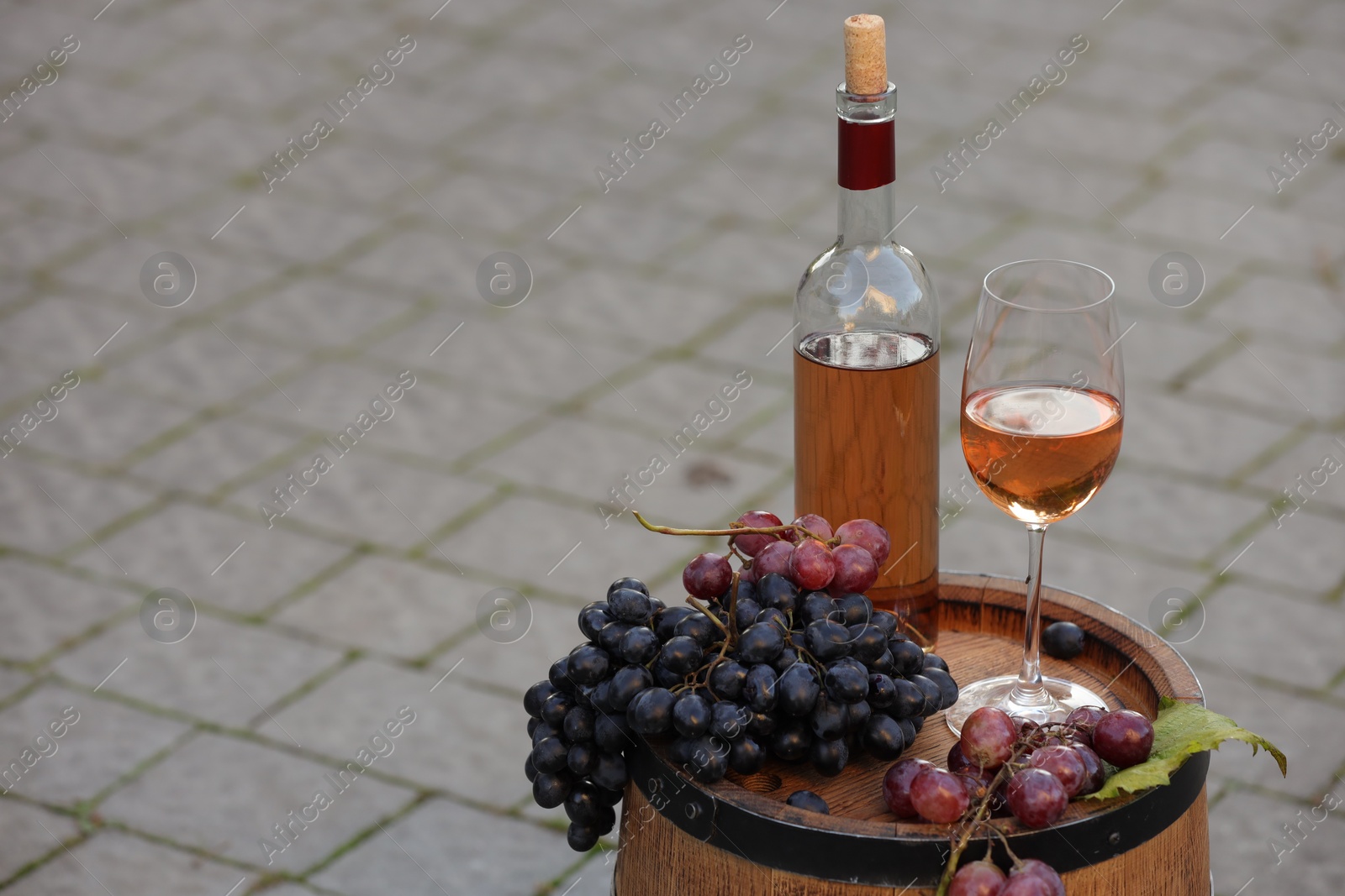 Photo of Delicious wine and ripe grapes on wooden barrel outdoors, space for text