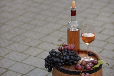 Photo of Delicious wine and ripe grapes on wooden barrel outdoors, space for text