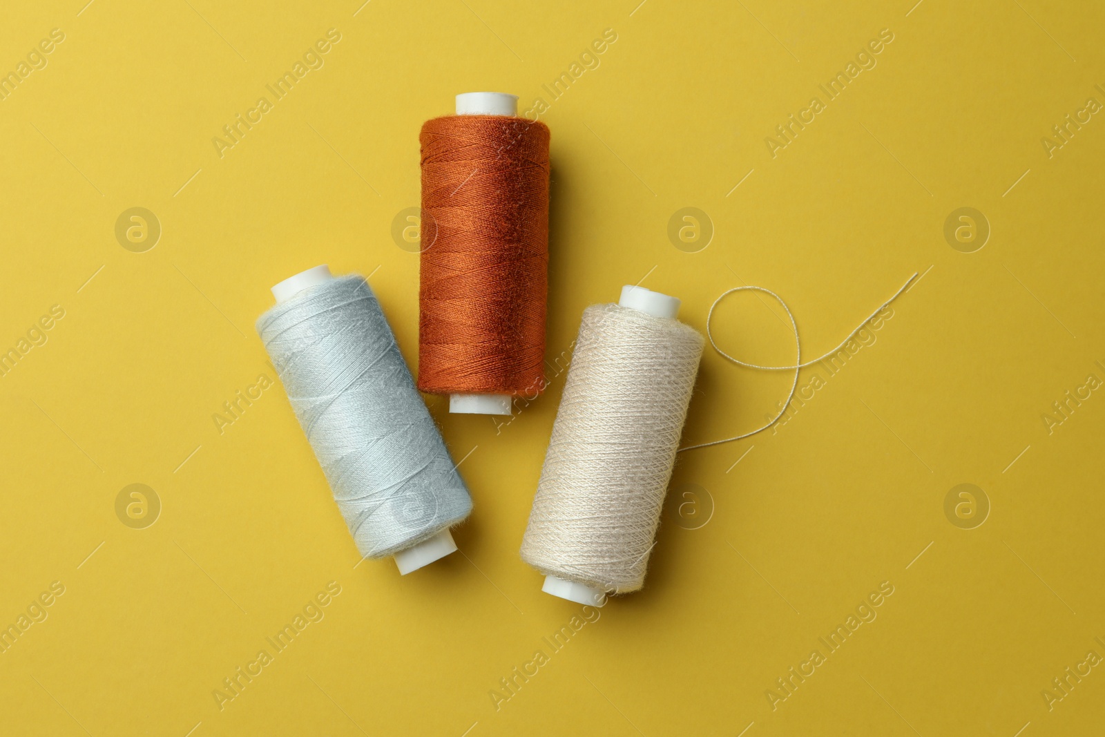 Photo of Different colorful sewing threads on yellow background, flat lay