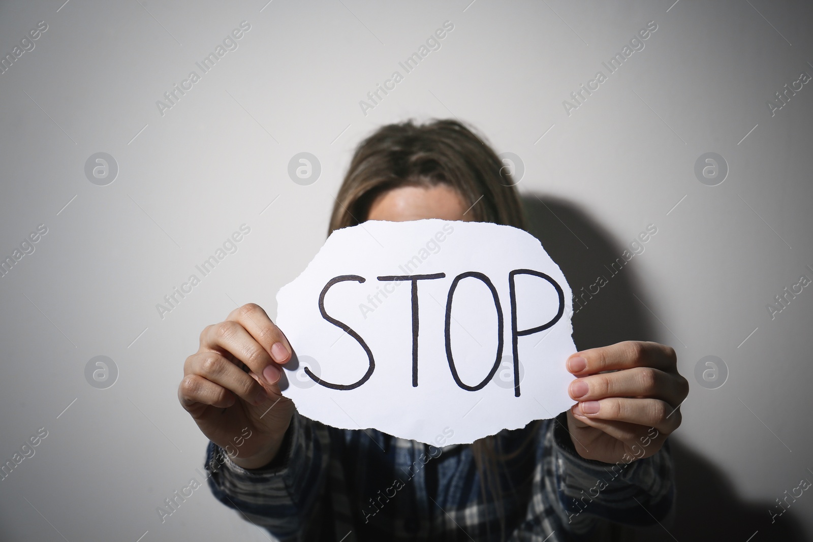 Photo of Abused young woman with sign STOP near white wall. Domestic violence concept