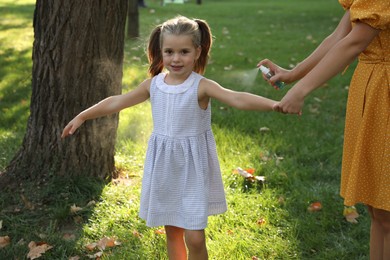 Mother applying insect repellent onto girl's hand in park