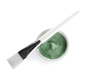Freshly made spirulina facial mask in bowl and brush on white background, top view