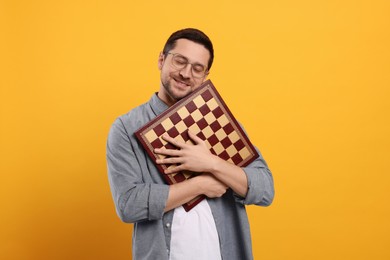 Handsome man holding chessboard on orange background