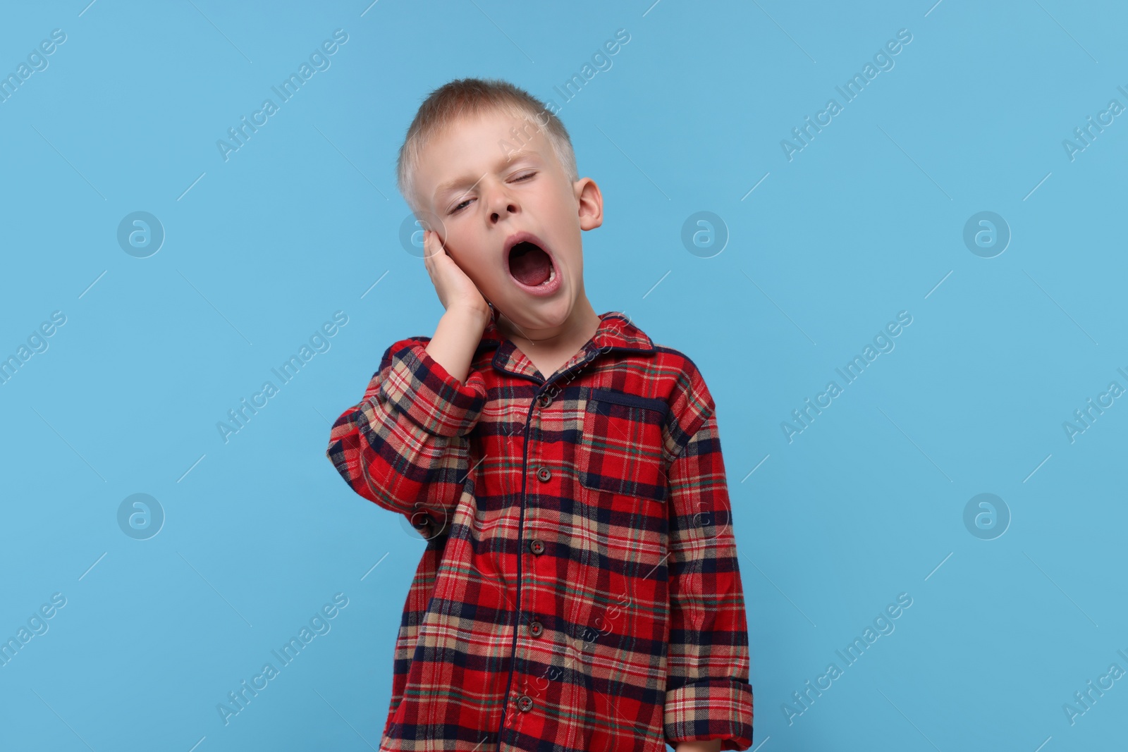 Photo of Sleepy boy yawning on light blue background. Insomnia problem