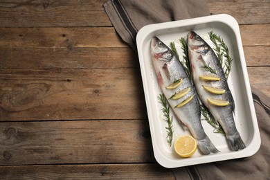 Photo of Baking tray with raw sea bass fish, lemon and rosemary on wooden table, top view. Space for text