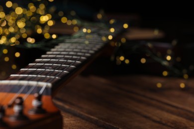 Photo of Closeup view of guitar on wooden table against blurred lights, space for text