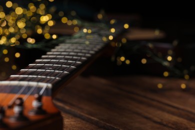 Closeup view of guitar on wooden table against blurred lights, space for text