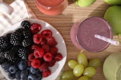 Photo of Glasses of different tasty smoothies and fresh ingredients on wooden table, flat lay