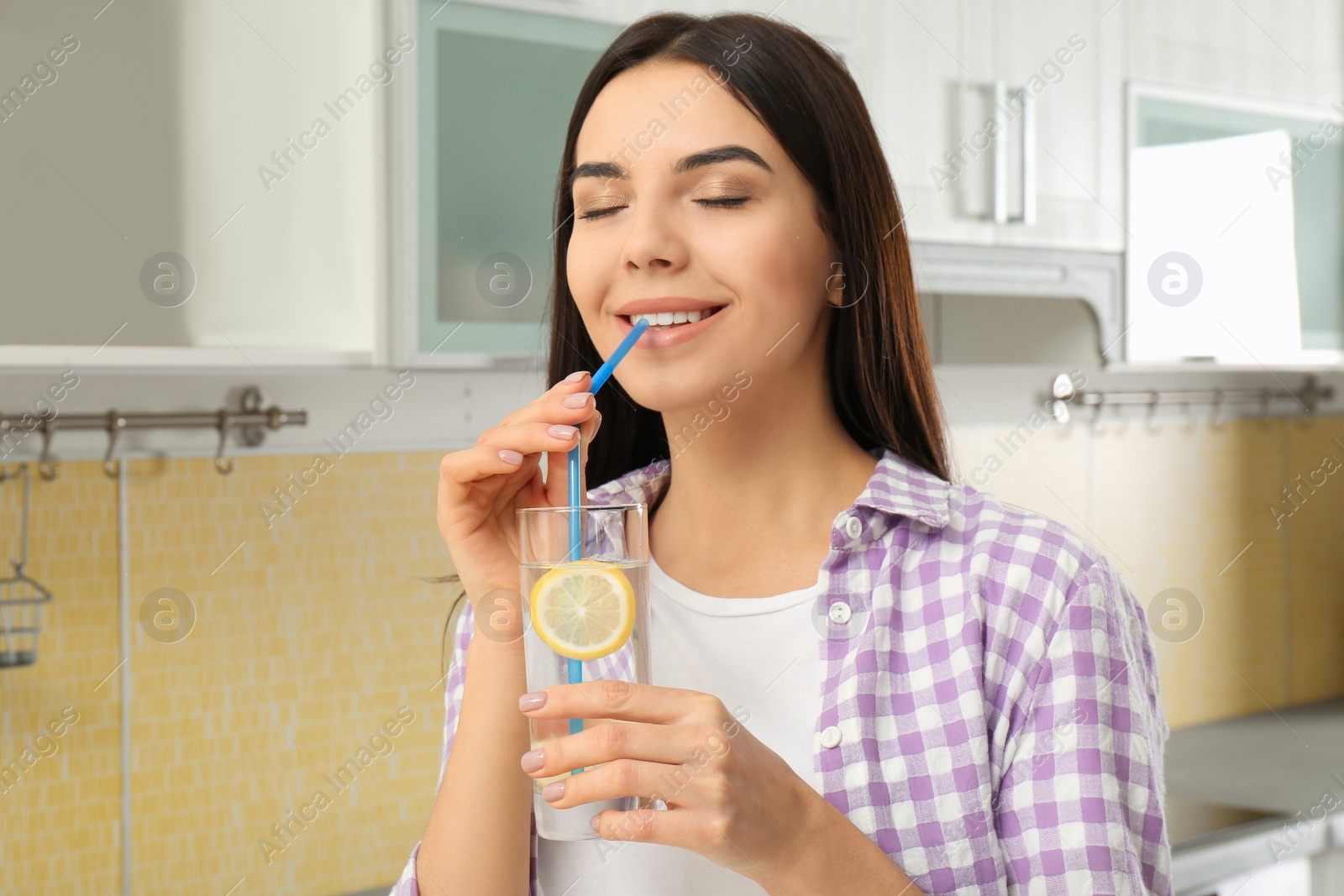 Photo of Beautiful young woman drinking lemon water in kitchen