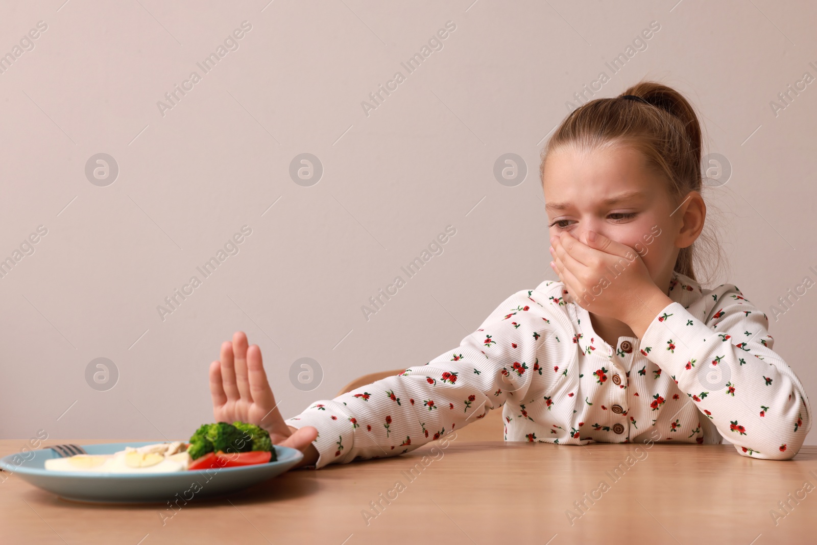 Photo of Cute little girl covering mouth and refusing to eat her dinner at table on grey background