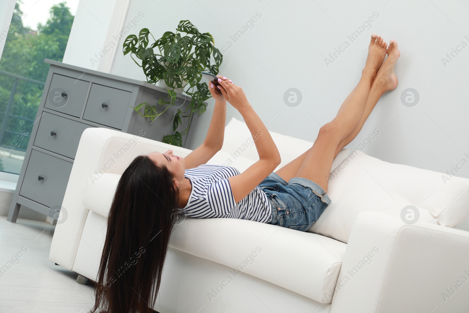 Photo of Young woman using smartphone on sofa at home. Internet shopping