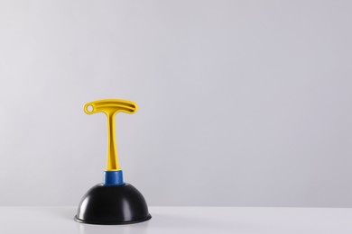 Photo of Plunger on white table against light grey background. Space for text