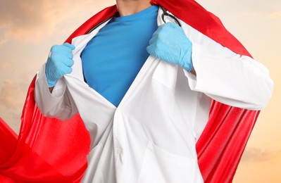 Image of Doctor wearing superhero cape taking uniform off against cloudy sky, closeup