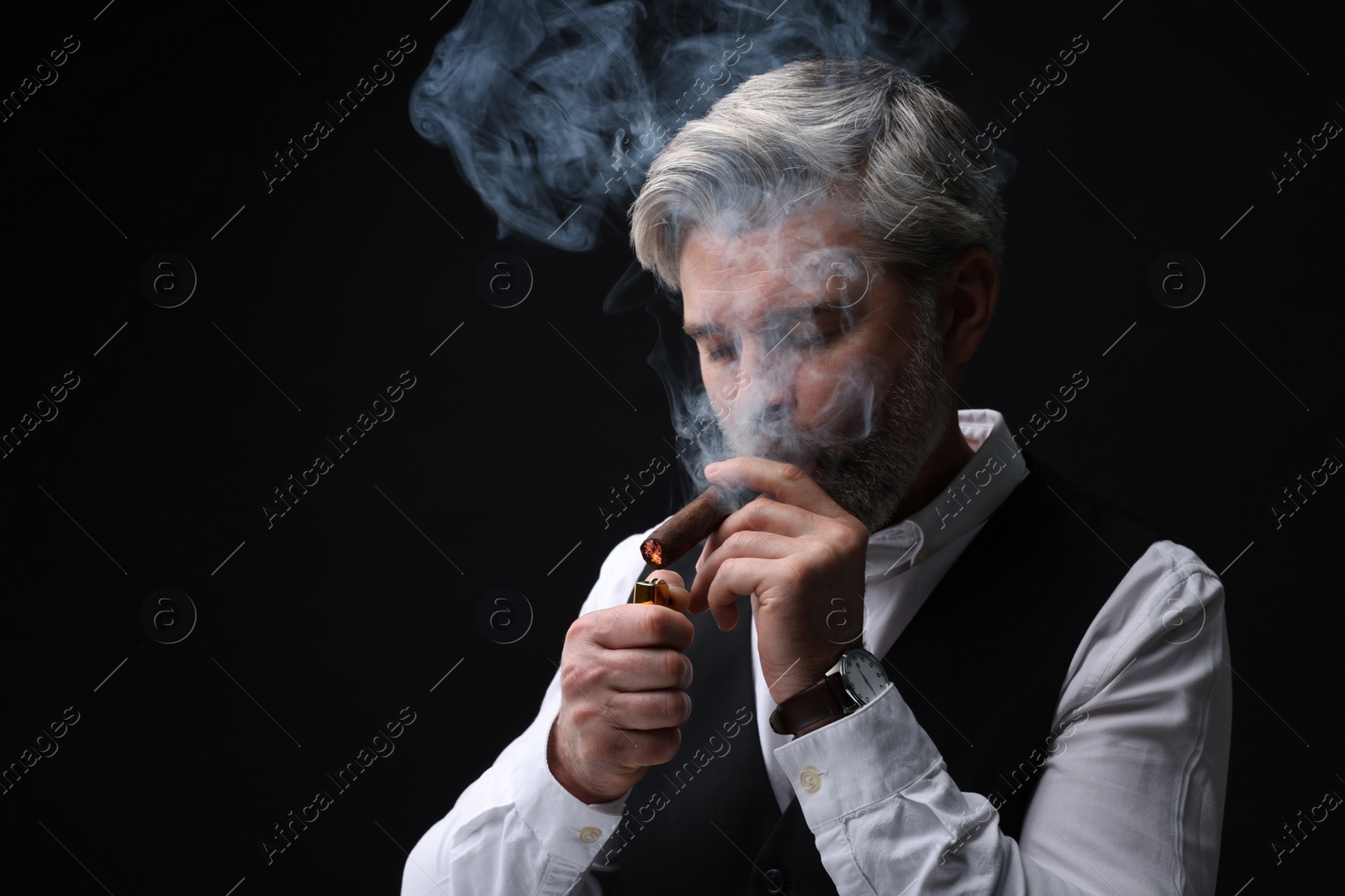 Photo of Bearded man lighting cigar on black background. Space for text