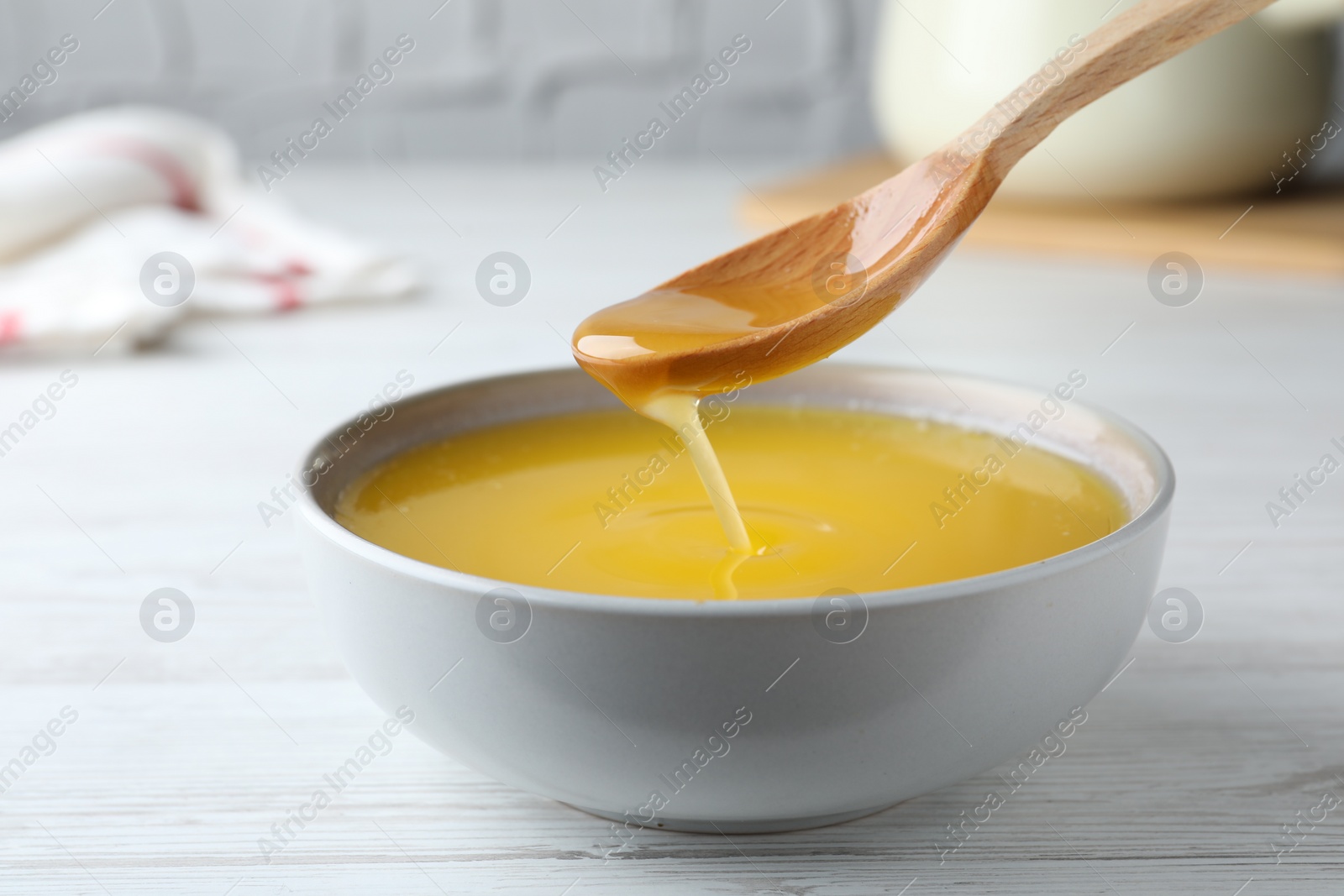 Photo of Spoon of clarified butter over bowl on white wooden table