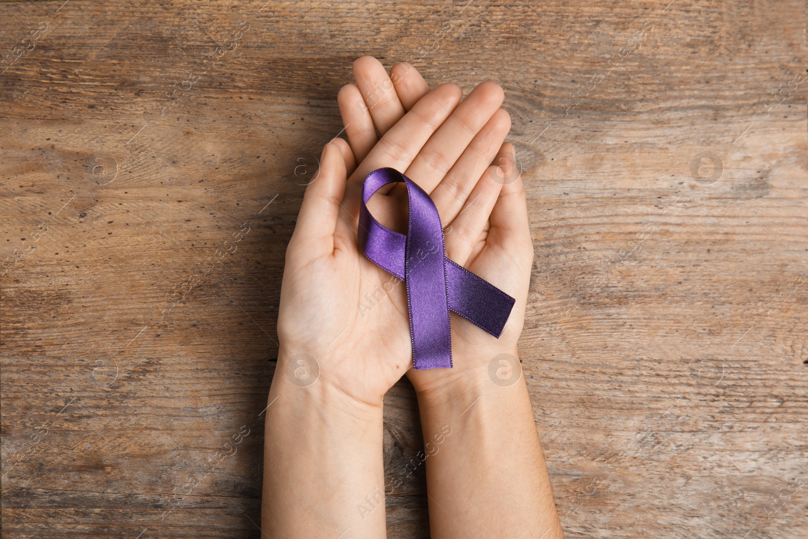 Photo of Woman holding purple ribbon on wooden background, top view. Domestic violence awareness