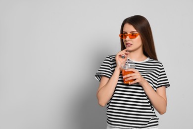 Photo of Beautiful young woman drinking juice from plastic cup on light grey background. Space for text