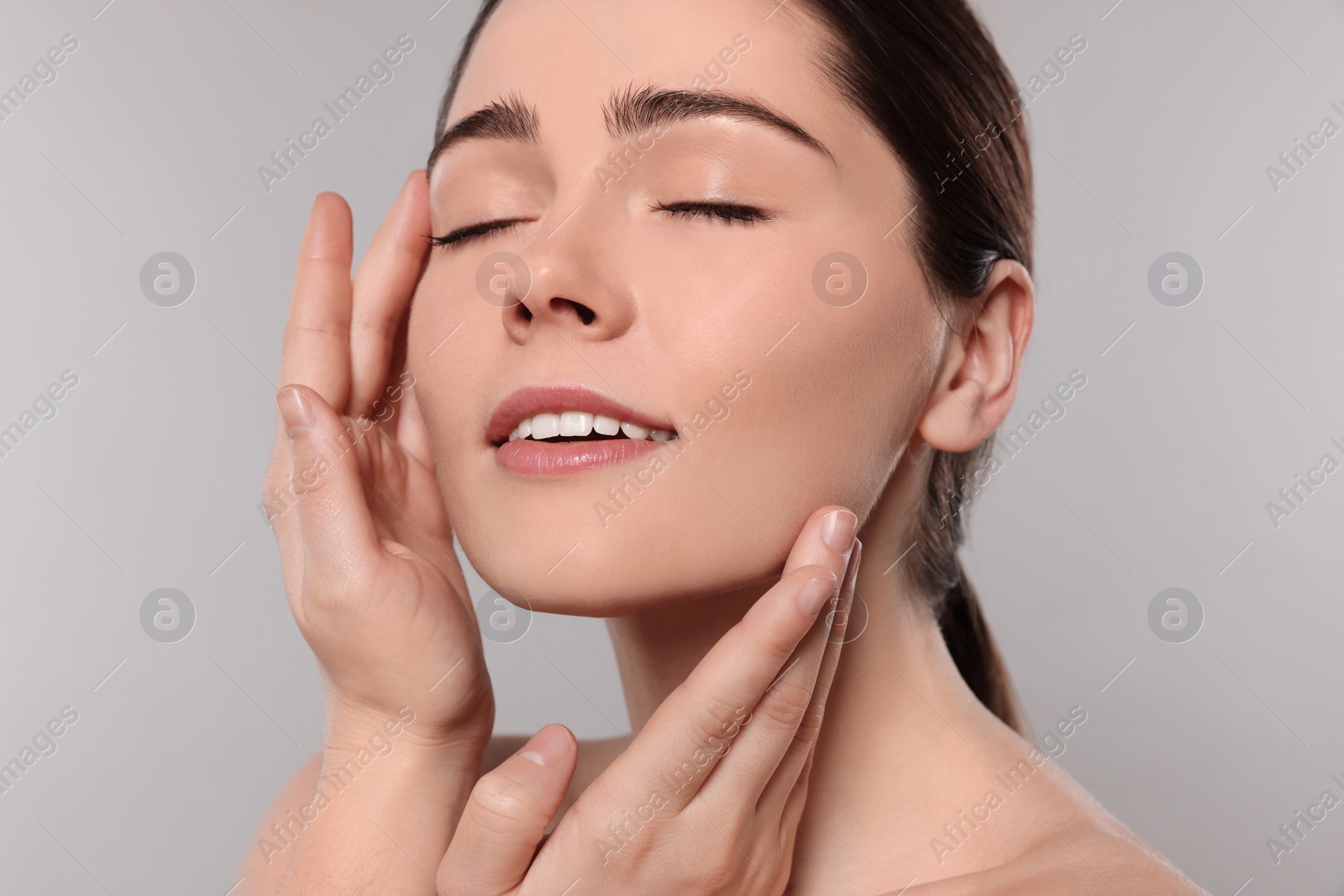 Photo of Young woman massaging her face on grey background