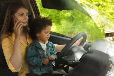 Photo of Mother with little daughter on knees driving car and talking by phone. Child in danger